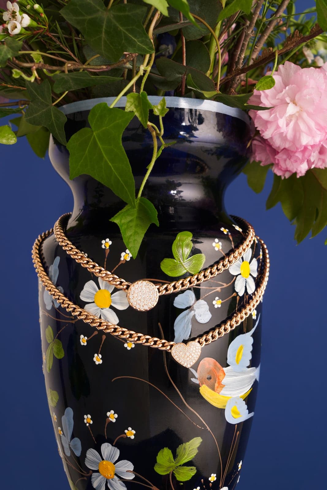Toledo gold chain necklaces draped over a floral painted vase